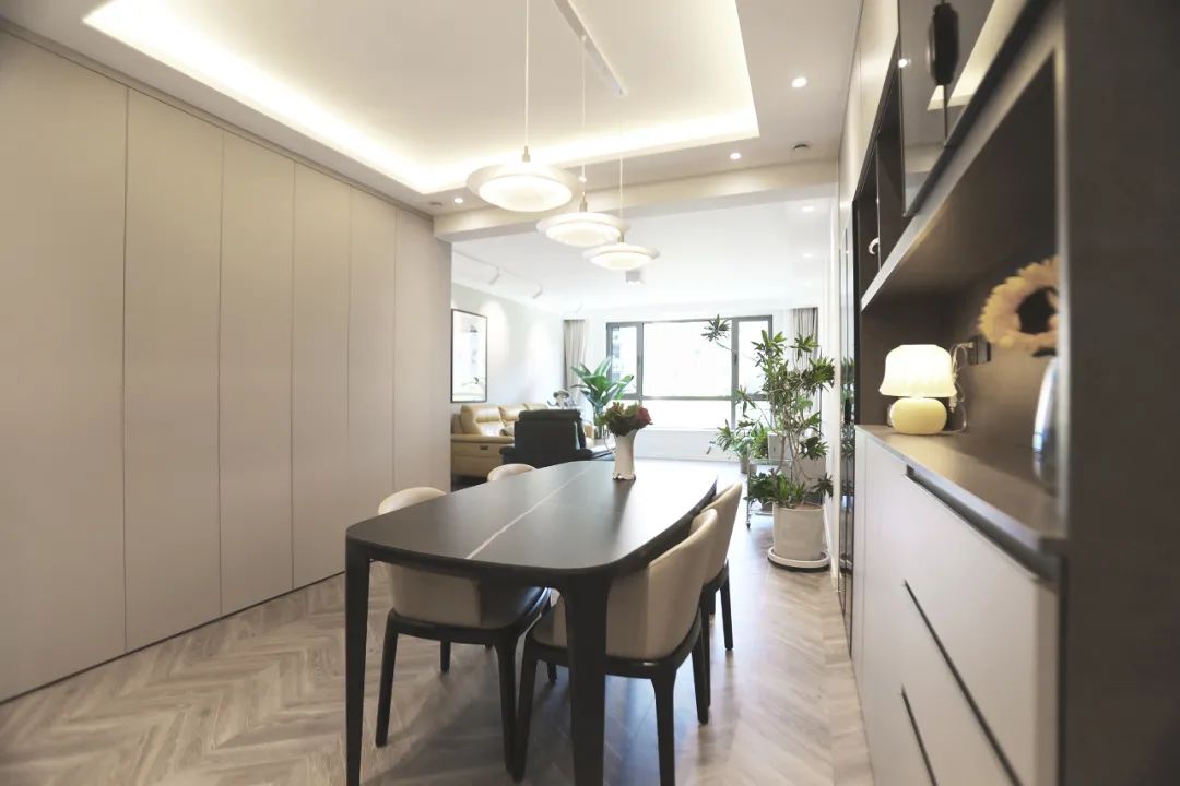 餐区与客厅之间有一道横梁，为了消解掉横梁的逼仄感，设计师做了经典的回字形吊顶+隐藏灯带配置，搭配餐桌前的三盏吊灯，让整个空间灯光富有层次。